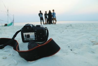 Camera at beach against friends during sunset