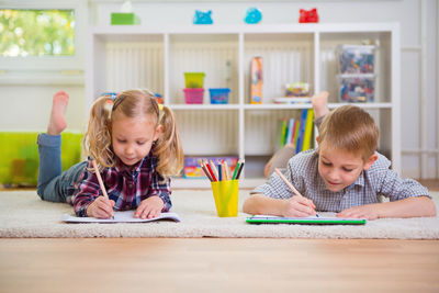 Cute sibling studying while lying on floor at home