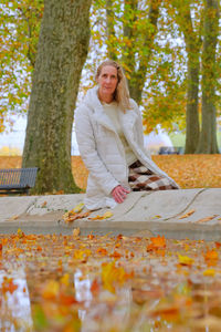 Portrait of woman standing by tree trunk during autumn