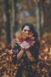 Young woman holding autumn leaf on field