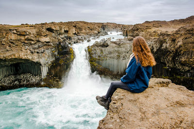 Side view of woman sitting on rock against waterfall
