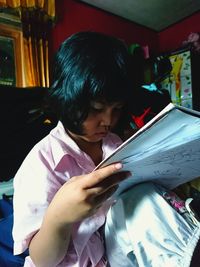 Rear view of boy holding book at home