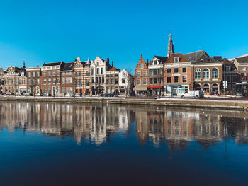 Reflection of buildings in lake against clear blue sky