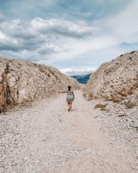 Rear view of man walking on rock against sky