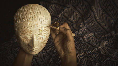 Cropped hand of woman carving mask