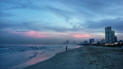 Scenic view of beach and buildings against sky at sunset