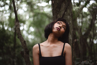 Portrait of young woman standing by tree trunk in forest