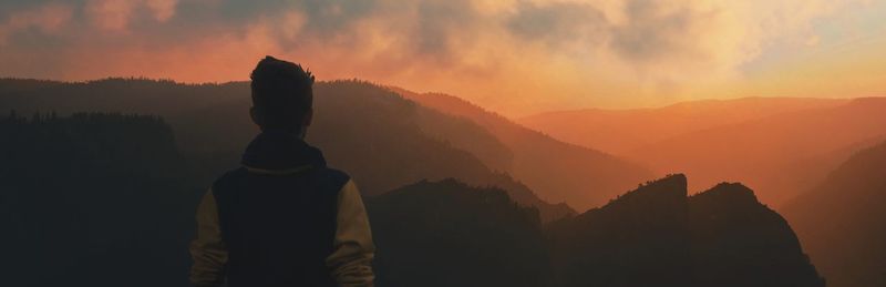 Panoramic view of man looking at mountains against sky during sunset