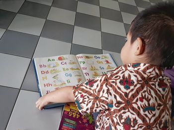 Rear view of boy reading book at home