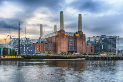 Buildings by river against cloudy sky