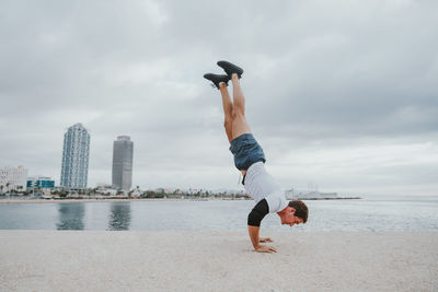 Side view of young woman exercising at beach against sky