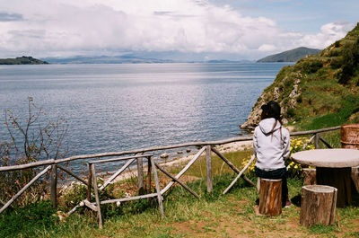 Rear view of woman standing by railing against sea