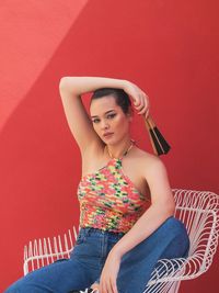 Portrait of beautiful young woman sitting on chair against red wall