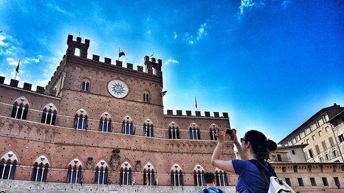 Low section of woman photographing building against blue sky