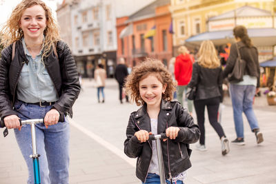 Portrait of mother and daughters playing with push scooter outdoors