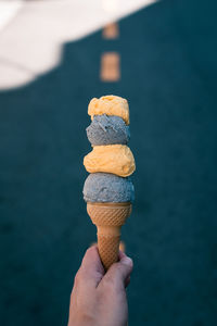 Cropped hand of person holding ice cream cone against road
