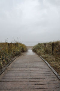 View of boardwalk leading towards shore against sky