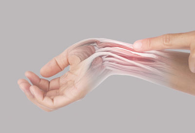 Close-up of hand holding cigarette over white background