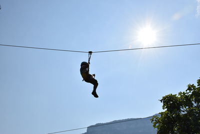 Low angle view of boy zip lining against clear sky