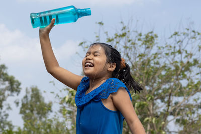 Young woman drinking water while standing against trees