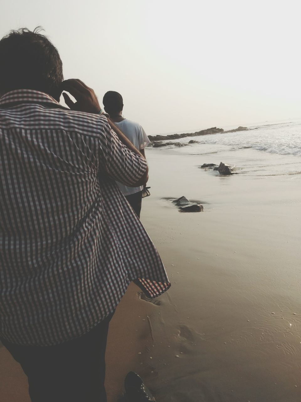 REAR VIEW OF PEOPLE AT BEACH AGAINST SKY