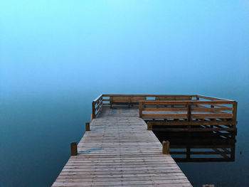 Empty pier over sea against clear blue sky