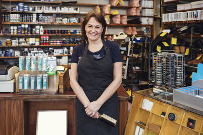 Portrait of happy shoemaker holding shoe brush while standing in shop