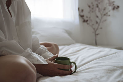 Close up of women's hands holding a cup of coffee on the bed.