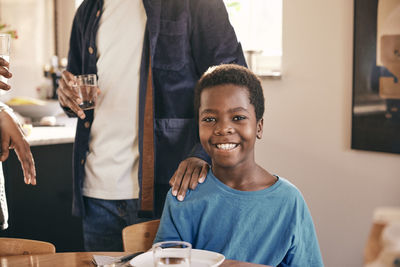 Portrait of happy boy with father keeping hand on shoulder at home