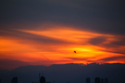 Silhouette of city against orange sky