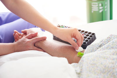 Midsection of nurse rubbing cotton on hand of patient at hospital