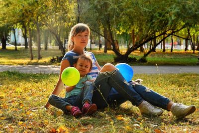 Full length of mother and girl sitting in park