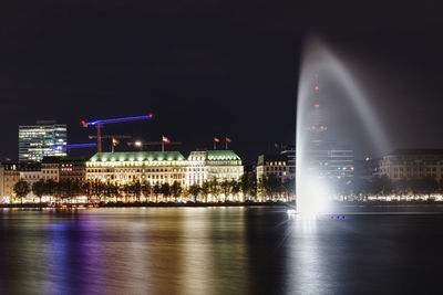 Fountain in a river against illuminated builduings at night