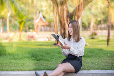 Happy businesswoman reading book while sitting at park