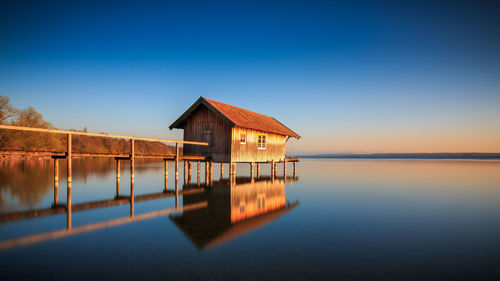 House by lake against clear blue sky