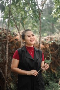 Portrait of young woman standing against trees