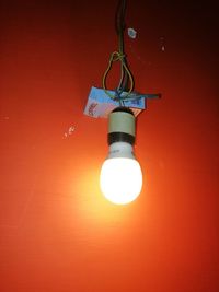 Low angle view of light bulb hanging against orange wall