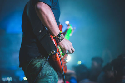 Midsection of man playing guitar while standing on stage