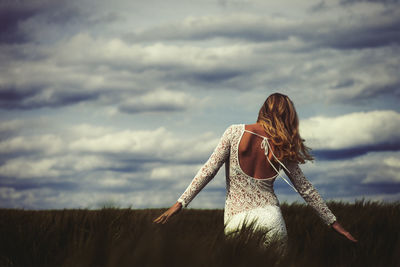 Rear view of woman standing on field against sky