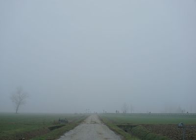 Road amidst field against sky during foggy weather