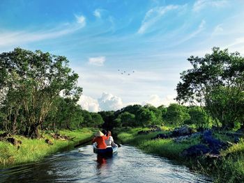 Rear view of people sitting on boat in river against sky