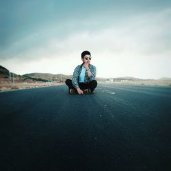 Portrait of young woman sitting on mountain against sky