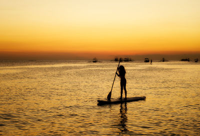 Silhouette of a girl floating on on the sup surfboard at amazing orange sunset over the sea