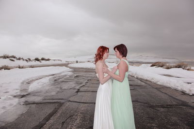 Sisters looking each other while standing on road against cloudy sky during winter