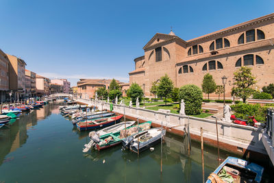 Boats moored in canal amidst buildings against clear blue sky