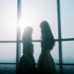 Side view of two girls standing against window
