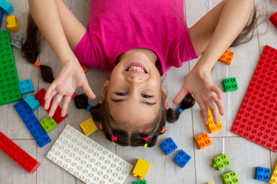 A funny little brunette girl in bright colorful clothes, lies on the floor with colorful toys