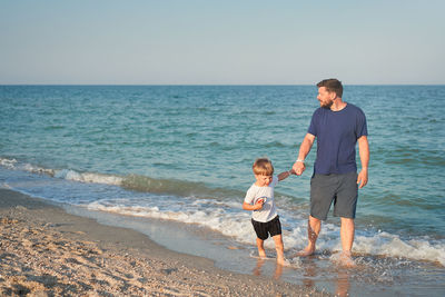 Full length of father and son on beach against sky