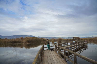 Pier over lake against sky and man with dog standing on a bridge 