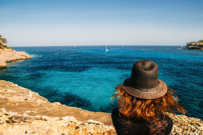 Rear view of woman in hat by sea against sky during sunny day